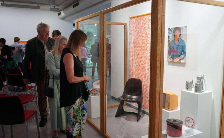 Besucherinnen und Besucher beim Betrachten der Vitrine mit Einrichtungs- und Gebrauchsgegenständen von 1975: Zum Vergrößern auf Bild klicken