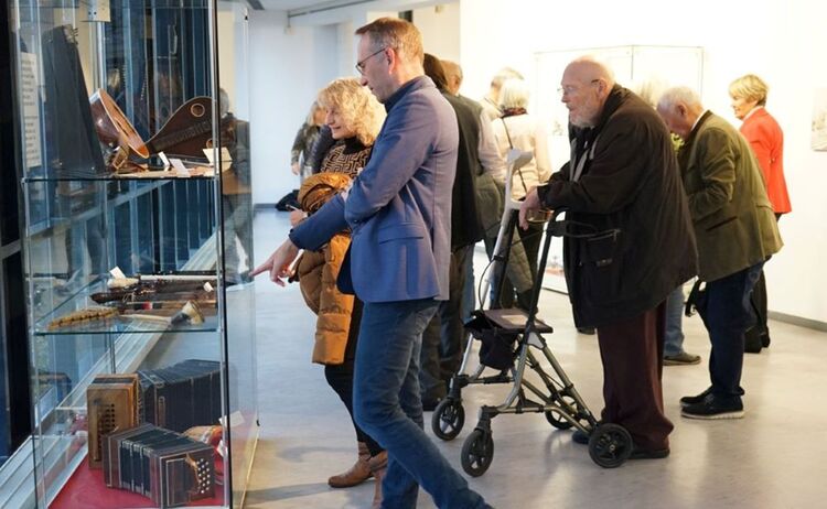 Erster Bürgermeister Robert Pötzsch im Gespräch mit einer Besucherin vor der Vitrine mit der Sammlung alter Musikinstrumente: Zum Vergrößern auf Bild klicken